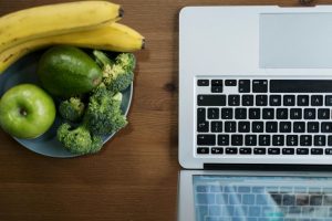 Flatlay of fresh fruits and vegetables with a laptop on a wooden table.
